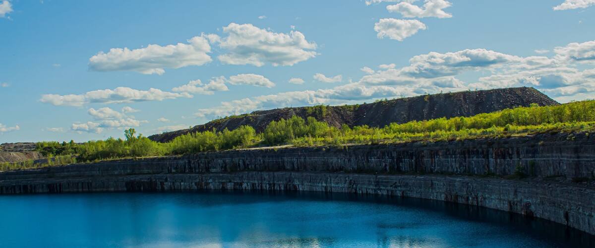 A calm blue lake with a rocky cliff and green vegetation in the background.