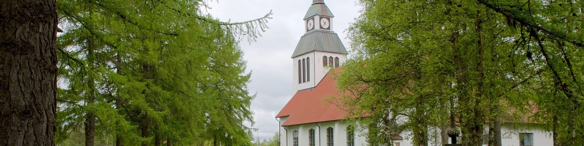 A church with a tall steeple and a clock tower, surrounded by trees and a well-maintained lawn.