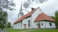 A church with a tall steeple and a cross, surrounded by trees and a grassy area.