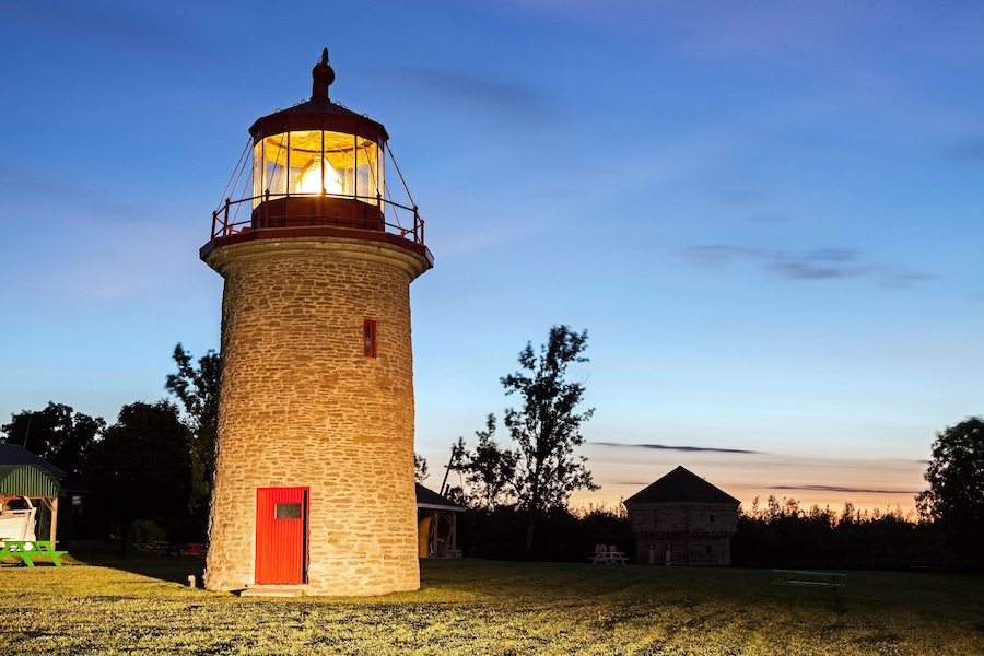 A lighthouse with a red door, surrounded by grass and trees.