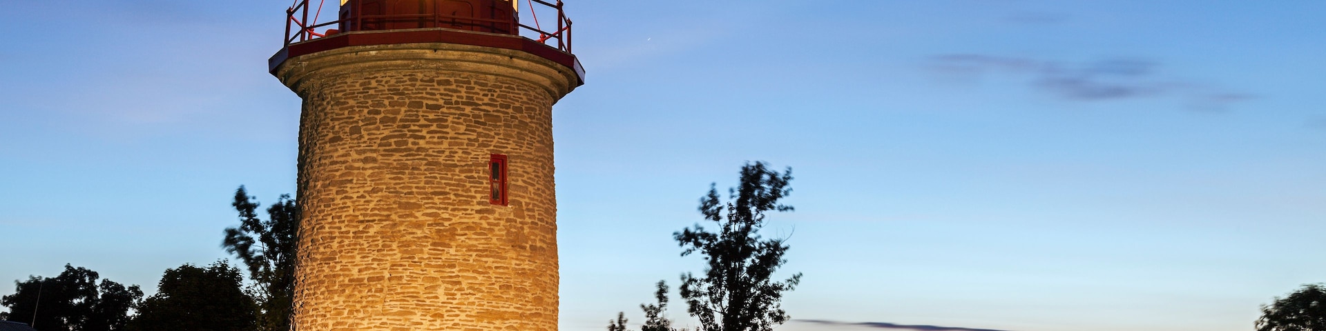 A lighthouse with a red door, surrounded by grass and trees.
