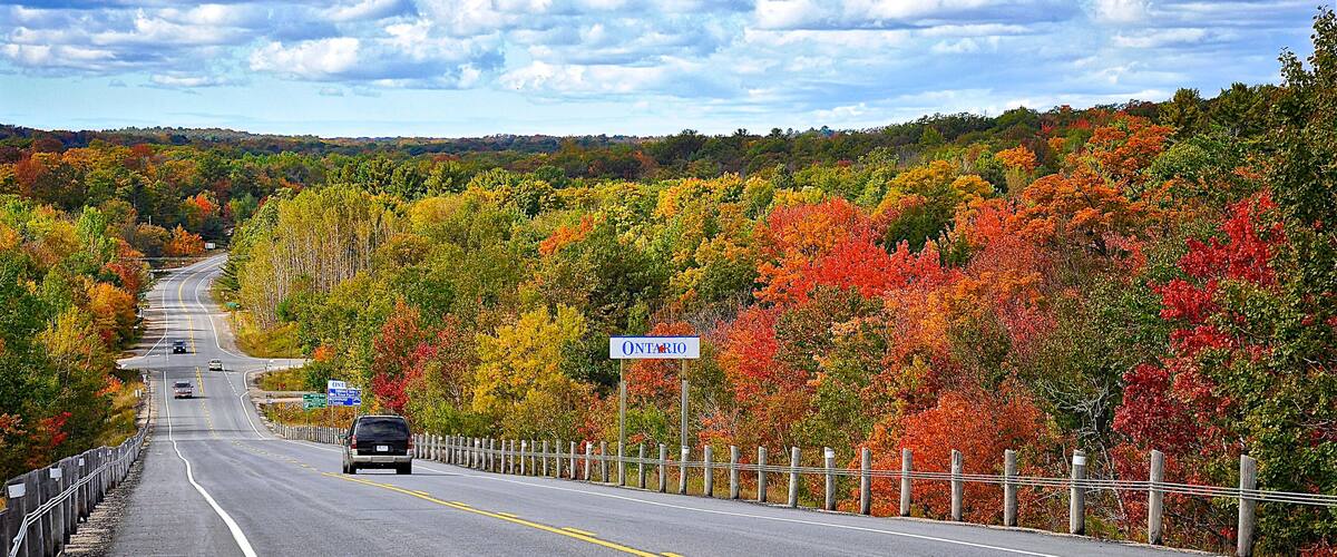 A highway with a sign for Ontario, surrounded by autumn foliage.