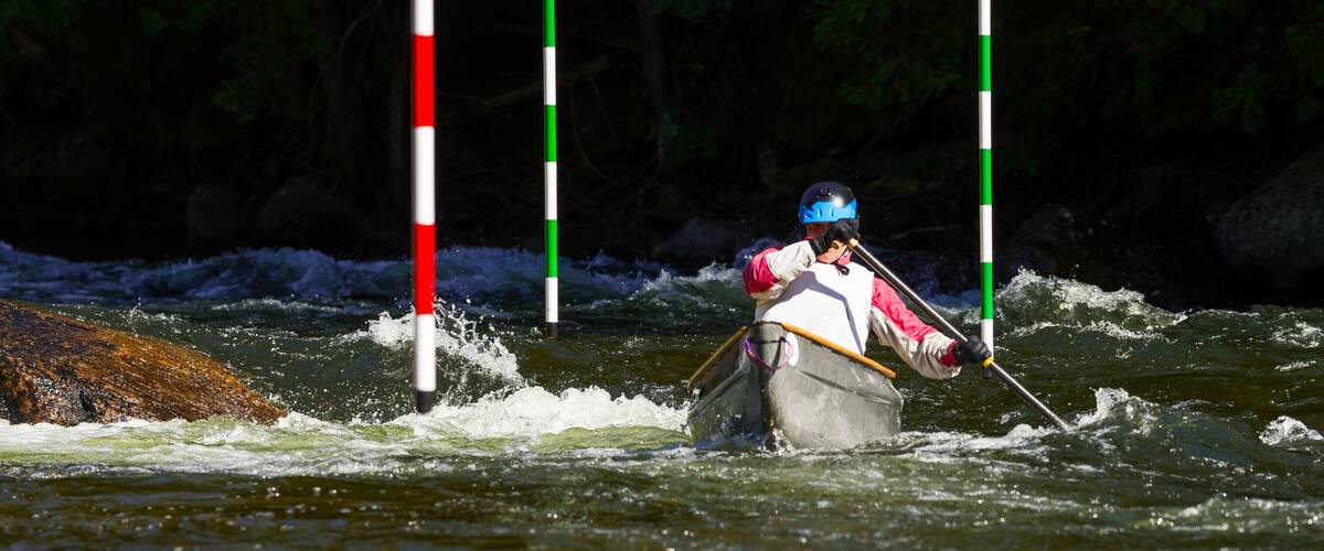 A kayaker navigating a river with white and green poles marking the course.