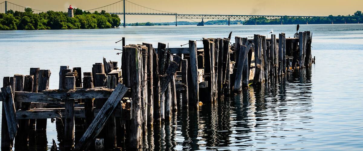 A wooden pier extending into calm water with a bridge and lighthouse in the background.