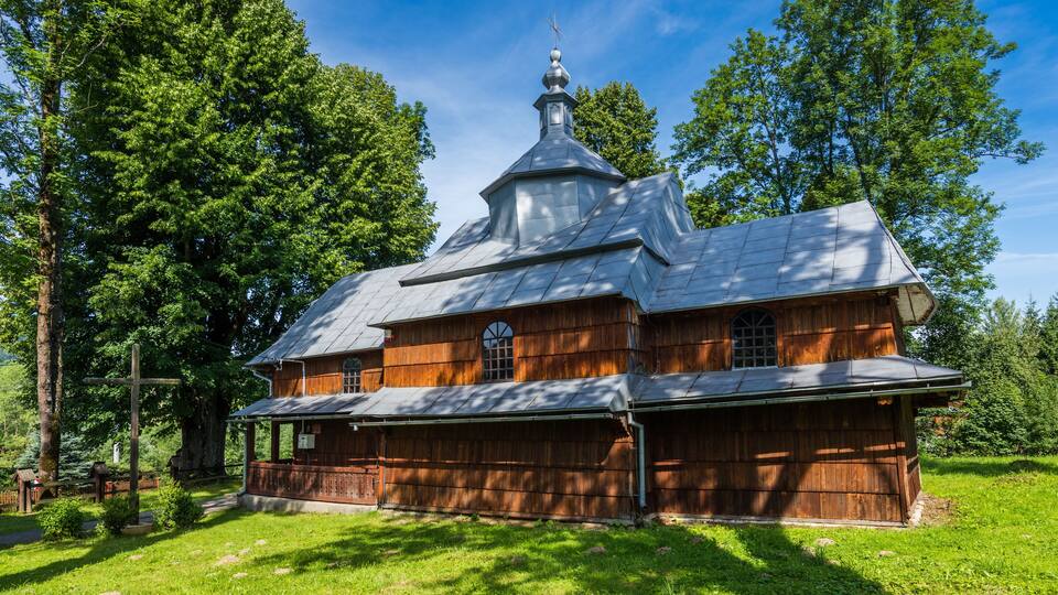 A wooden church with a bell tower and crosses in a forested area.