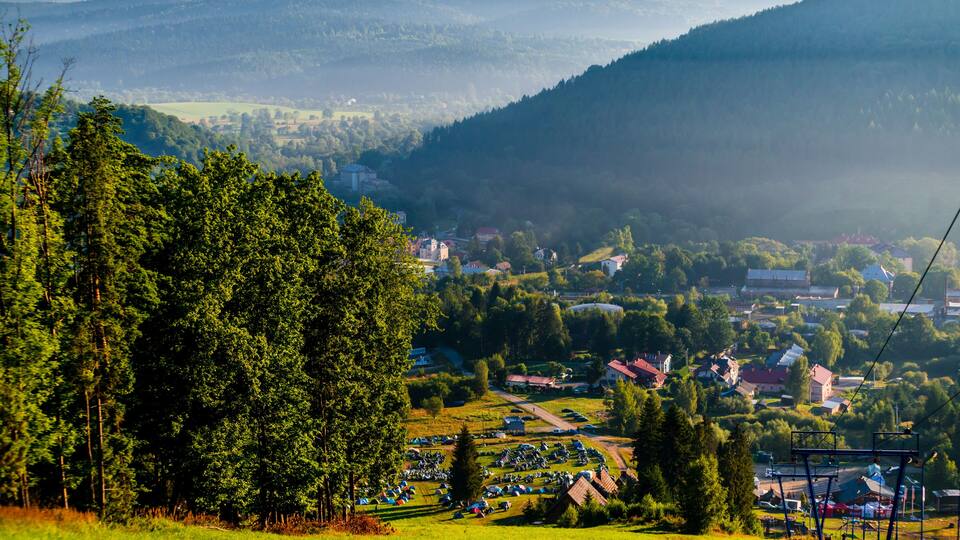 A mountainous landscape with a village nestled in the valley, surrounded by dense forests and a clear sky.