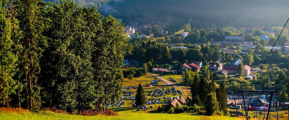 A mountainous landscape with a village nestled in the valley, surrounded by dense forests and a clear sky.
