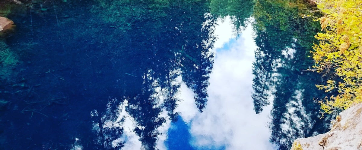A clear blue lake surrounded by dense green forest and rocky terrain.
