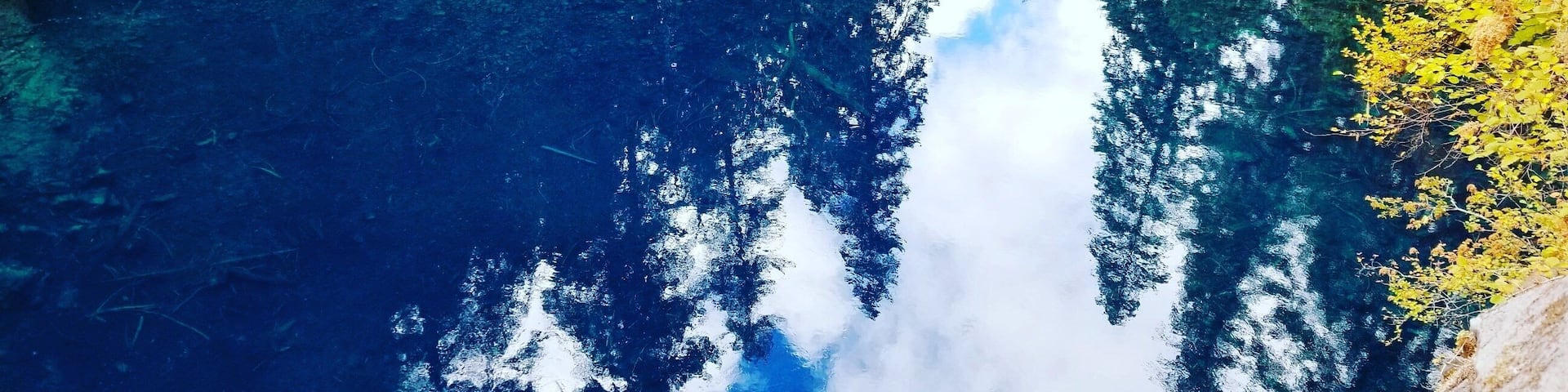 A clear blue lake surrounded by dense green forest and rocky terrain.