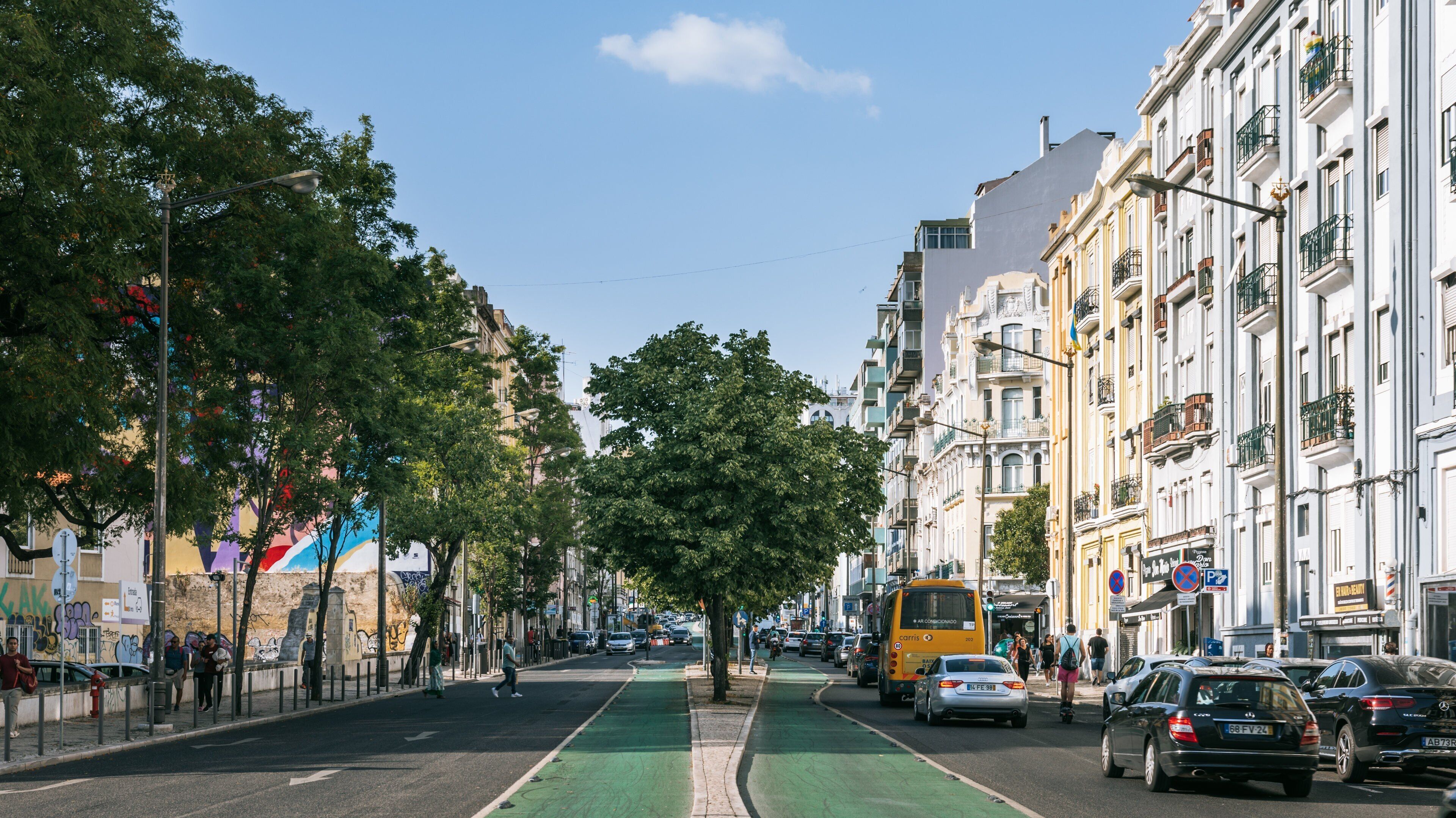 A city street with a green bike lane, parked cars, and a yellow bus.