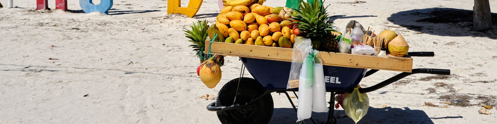 carreton con fruta en una playa paradisiaca con unas letras de colores detras