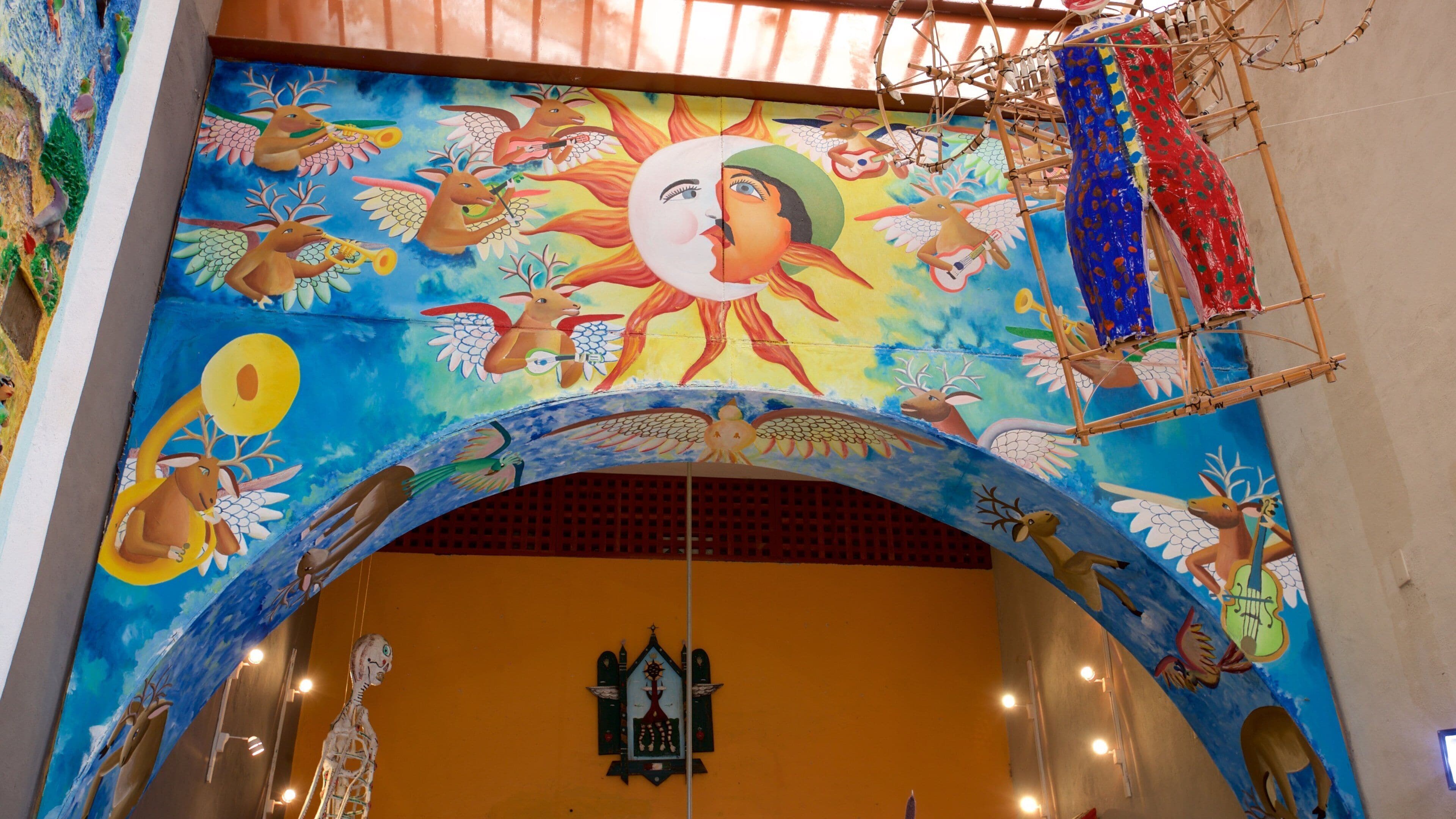 Un mural vibrante con un sol central, rodeado de diversas figuras y animales.