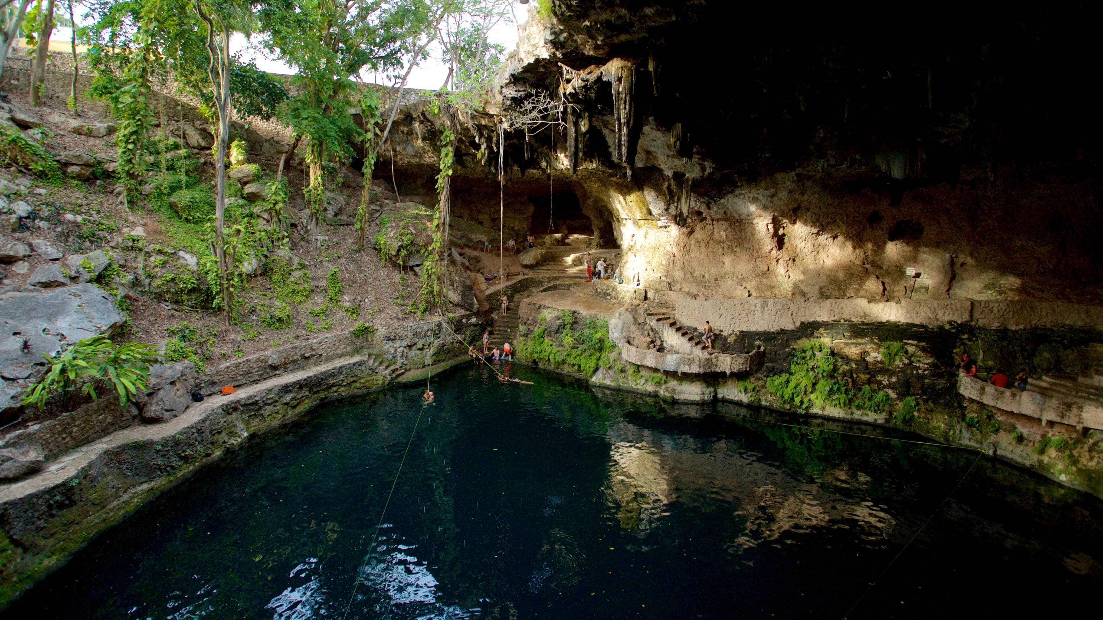 Une grotte avec une mare, des parois rocheuses et des stalactites pendant du plafond.