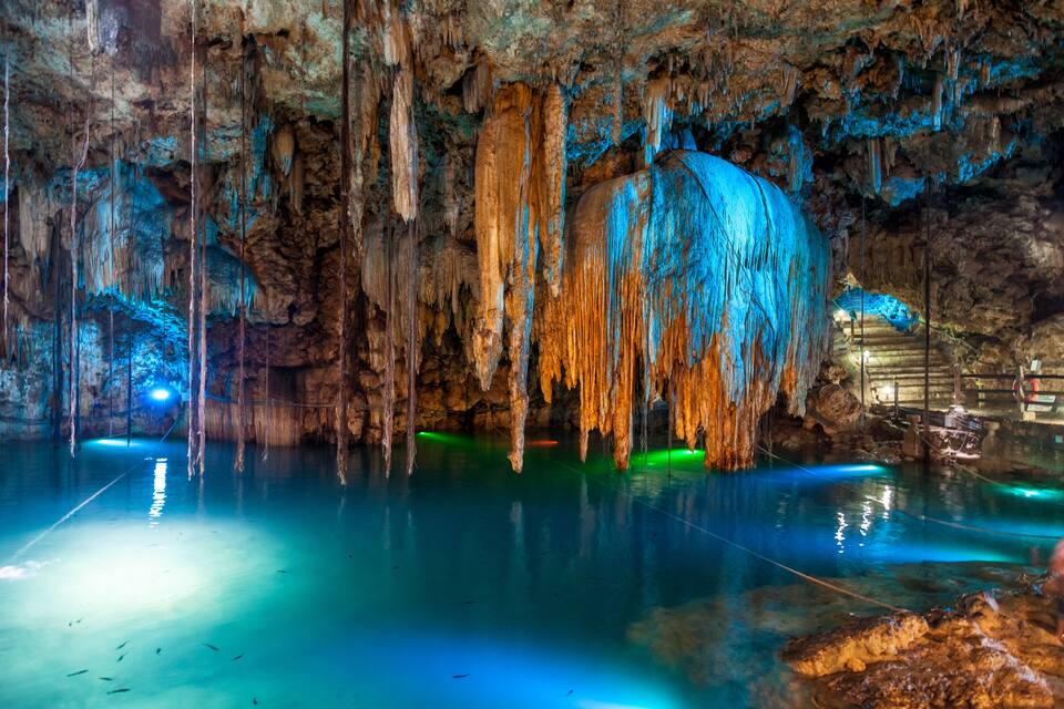 Una cueva con estalactitas y estalagmitas, iluminada por luces azules y verdes.