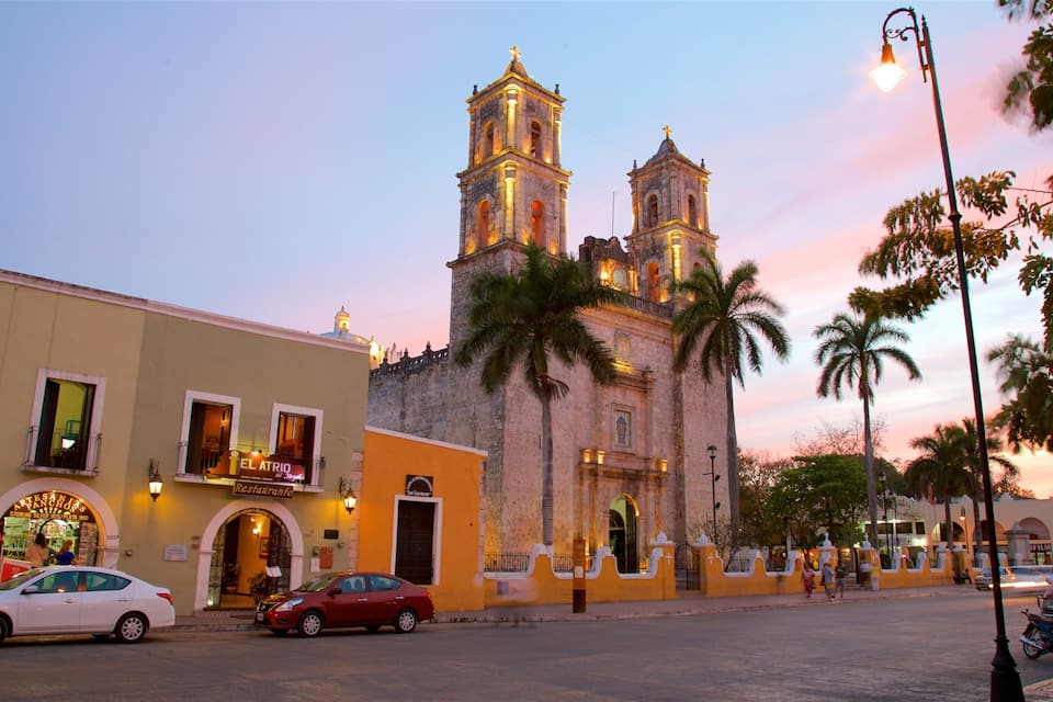A historic church with two towers, a street with cars, and palm trees.