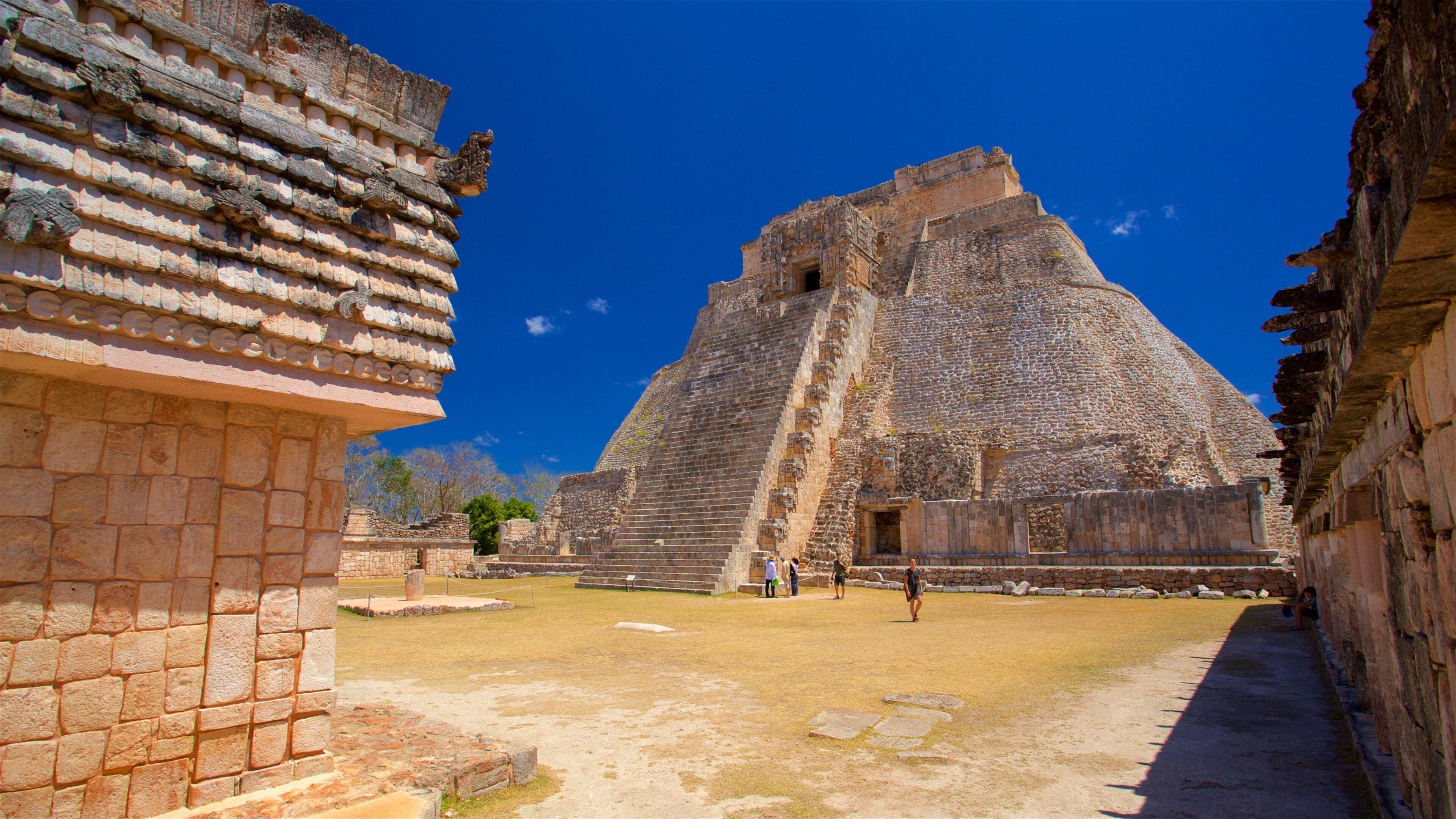 A large stone pyramid with a stepped structure, surrounded by stone walls and a clear blue sky.