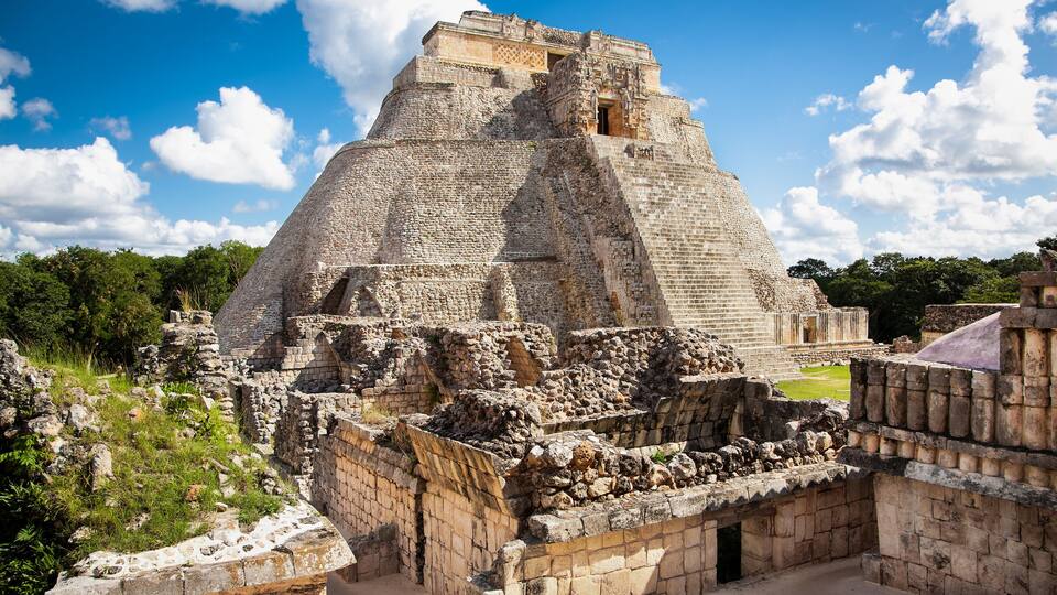 An ancient pyramid structure with surrounding ruins, set against a clear blue sky.