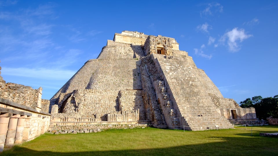 A large pyramid structure with a staircase leading to the top, surrounded by a grassy area and a clear blue sky.