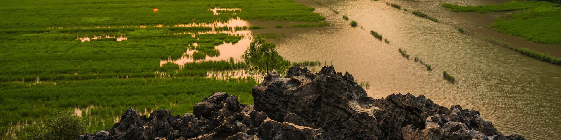 A river winding through lush green fields and limestone karsts under a setting sun.