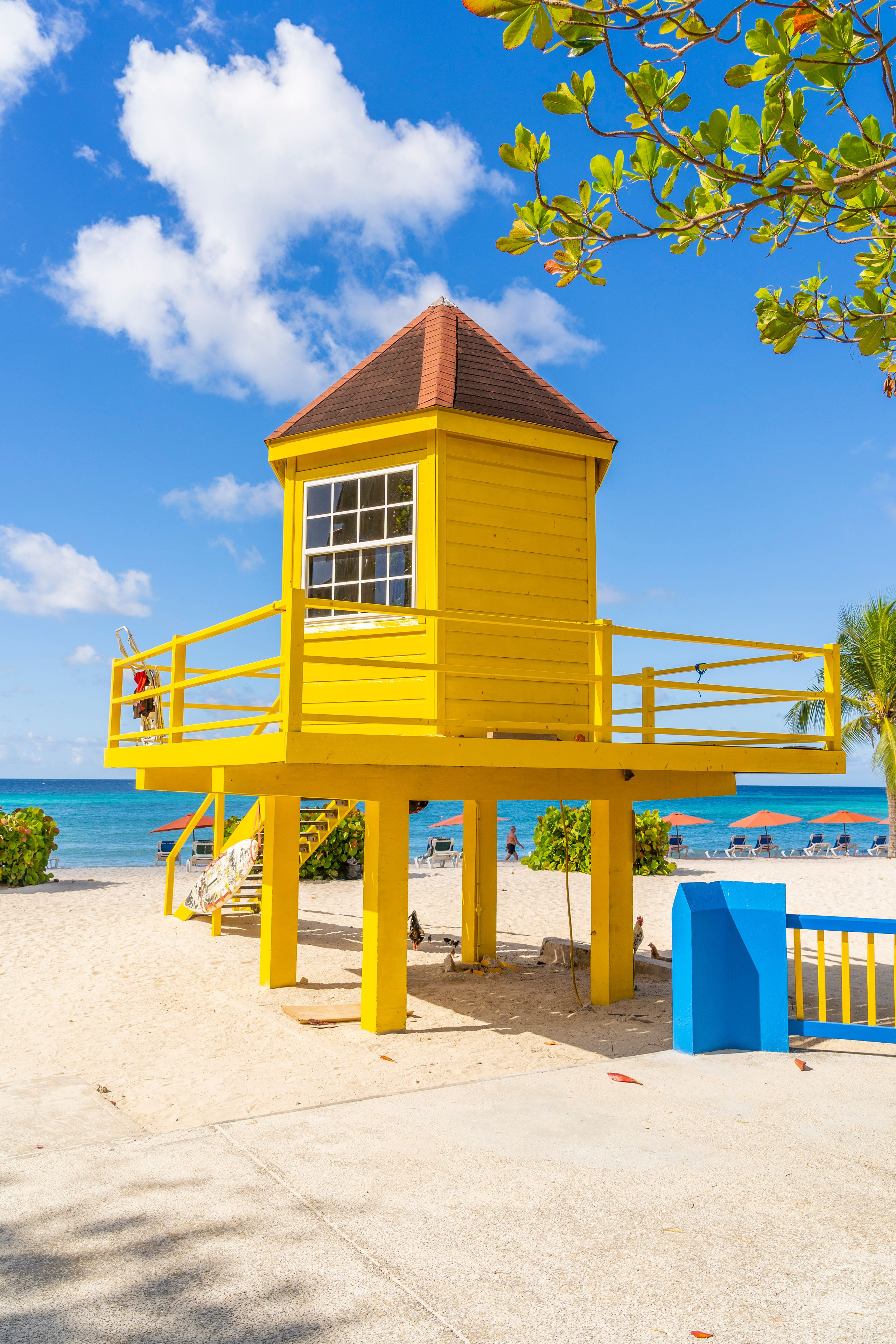 Una torre de salvavidas amarilla en una playa, con cielos azules despejados y el océano al fondo.