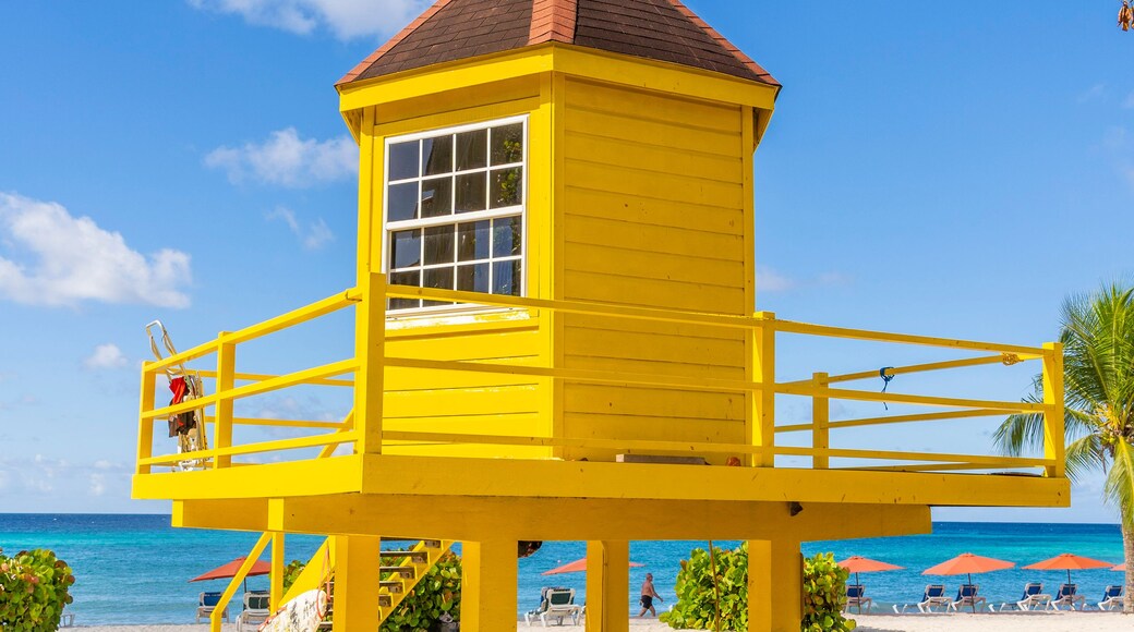 Una torre de salvavidas amarilla en una playa, con cielos azules despejados y el océano al fondo.