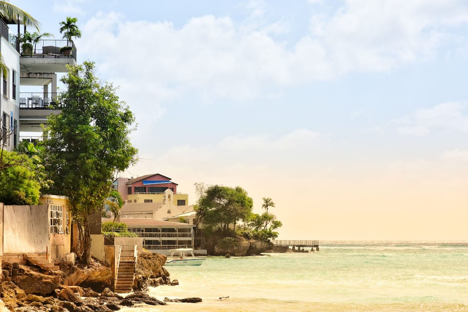 A coastal scene with a building, palm trees, and a pier extending into the ocean.