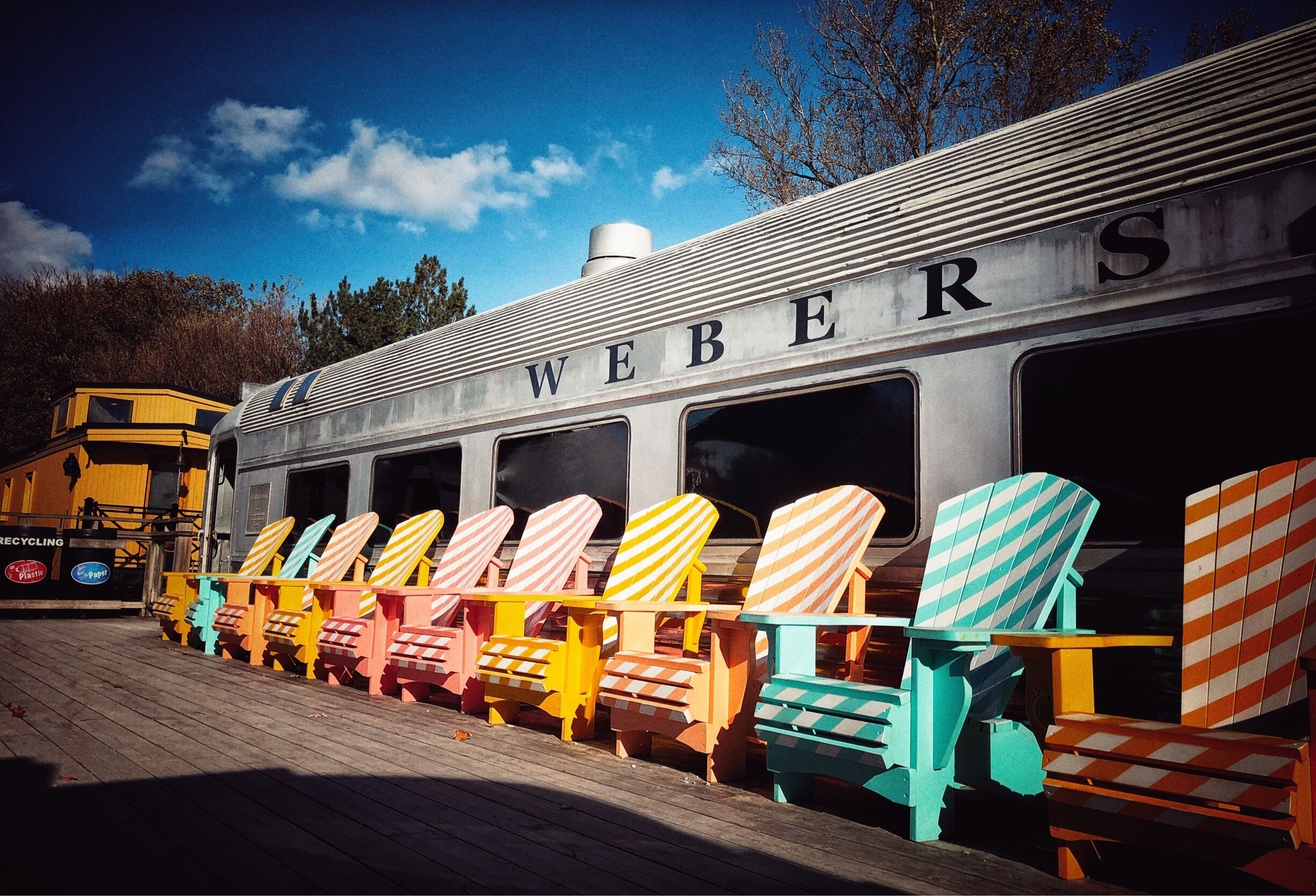 A train with colorful Adirondack chairs lined up in front.