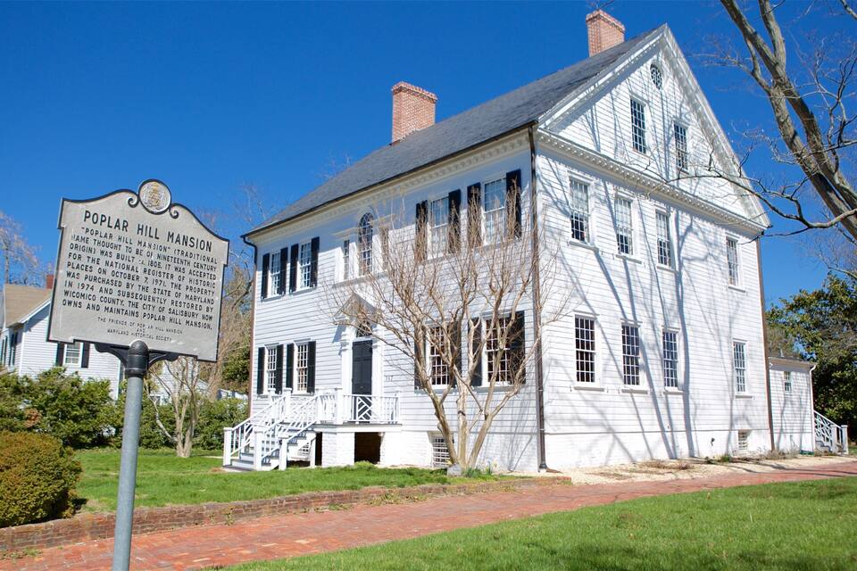 A historic white mansion with a sign in front.