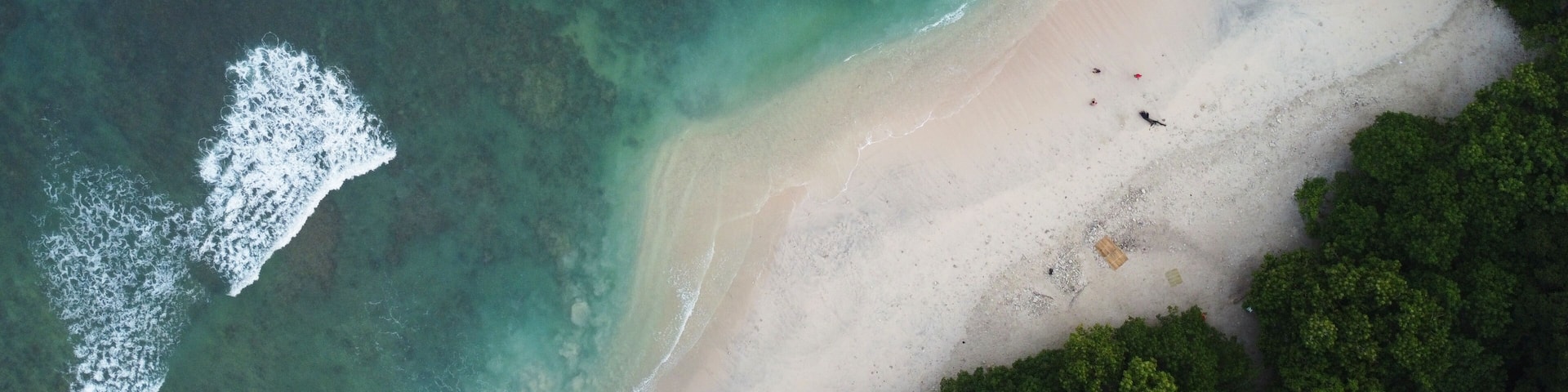 An aerial view of a beach with clear turquoise waters, a sandy shore, and a small boat.