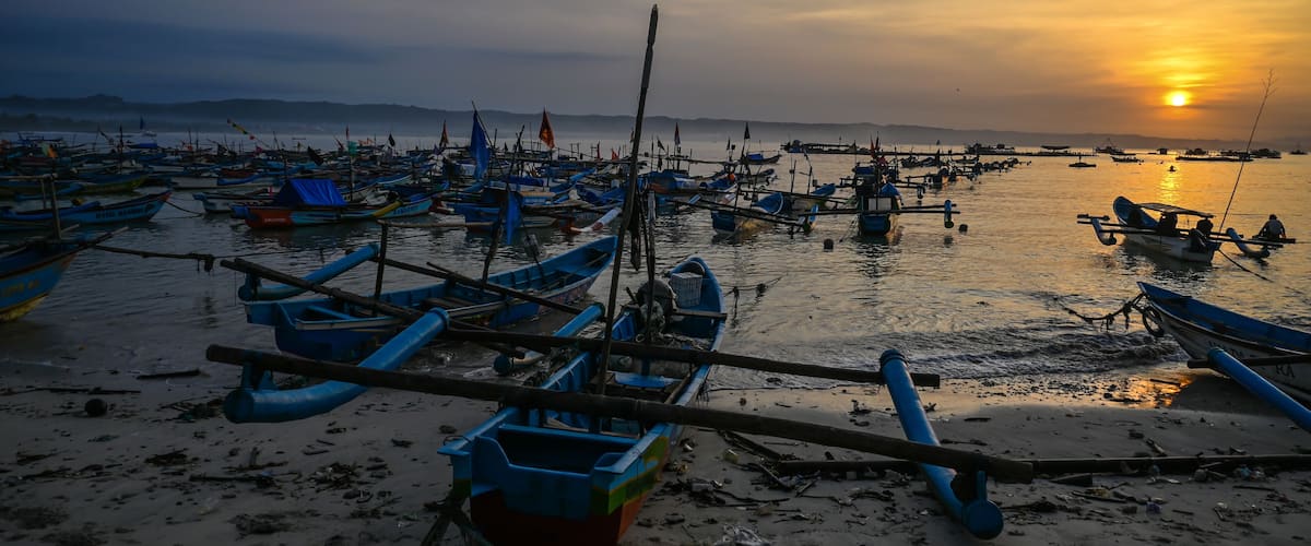A harbor at sunset with numerous boats docked and a calm sea.