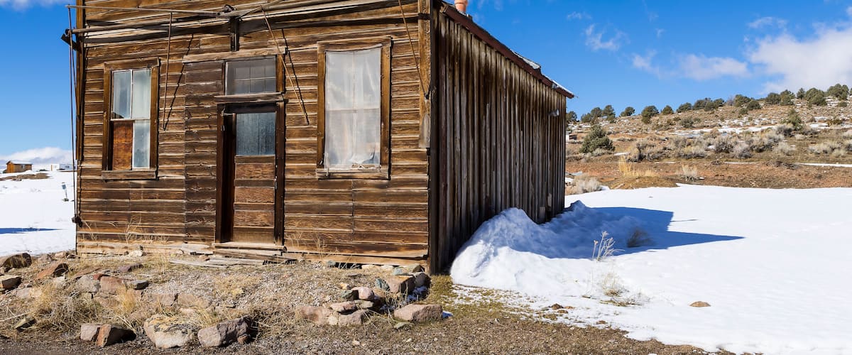 A wooden cabin with a chimney, surrounded by snow and a clear blue sky.