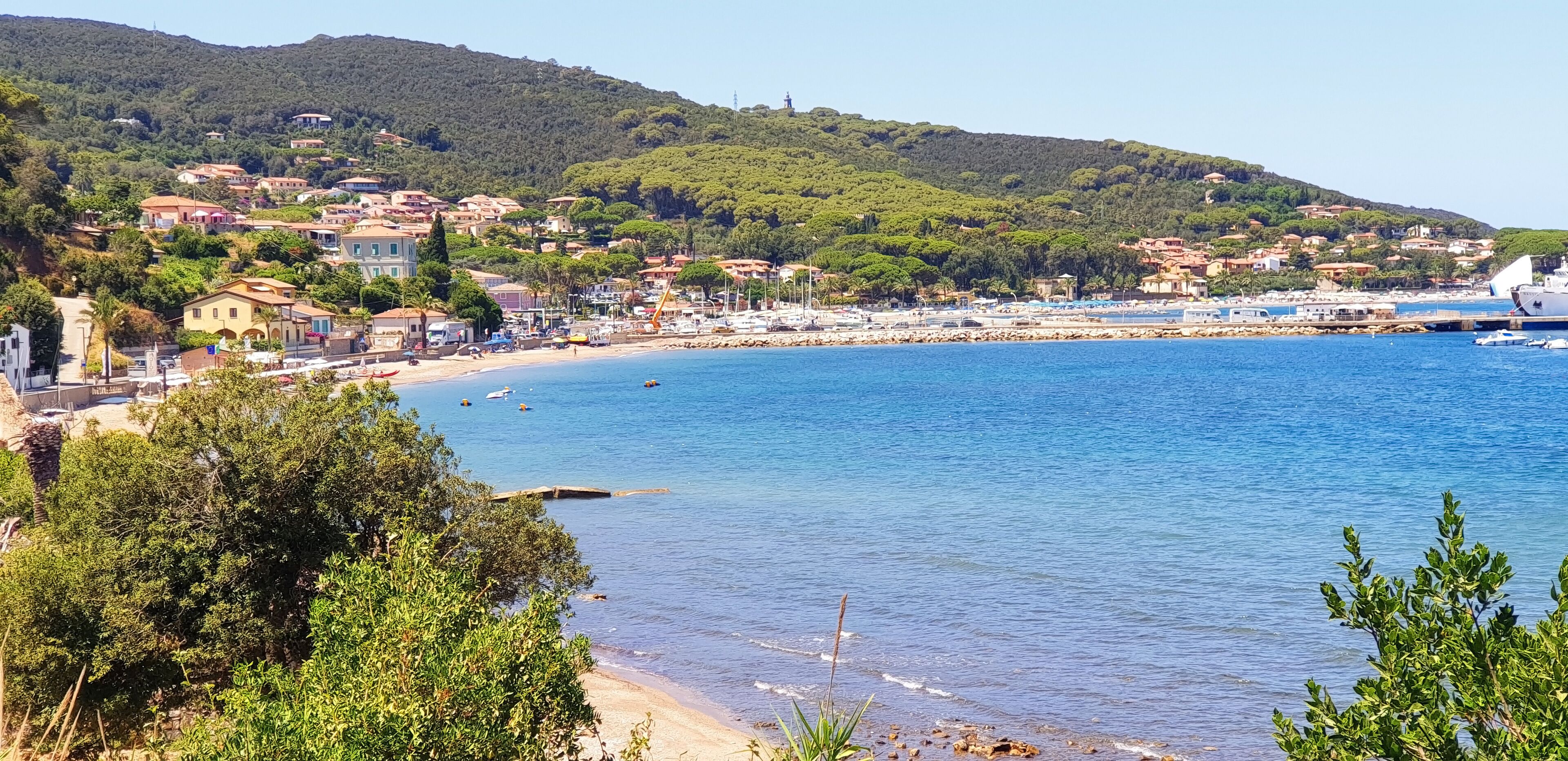 A coastal town with a beach, boats, and a hilly backdrop.