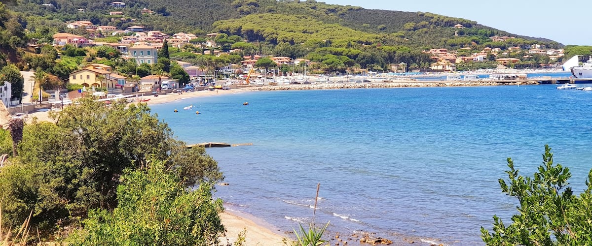 A coastal town with a beach, boats, and a hilly backdrop.