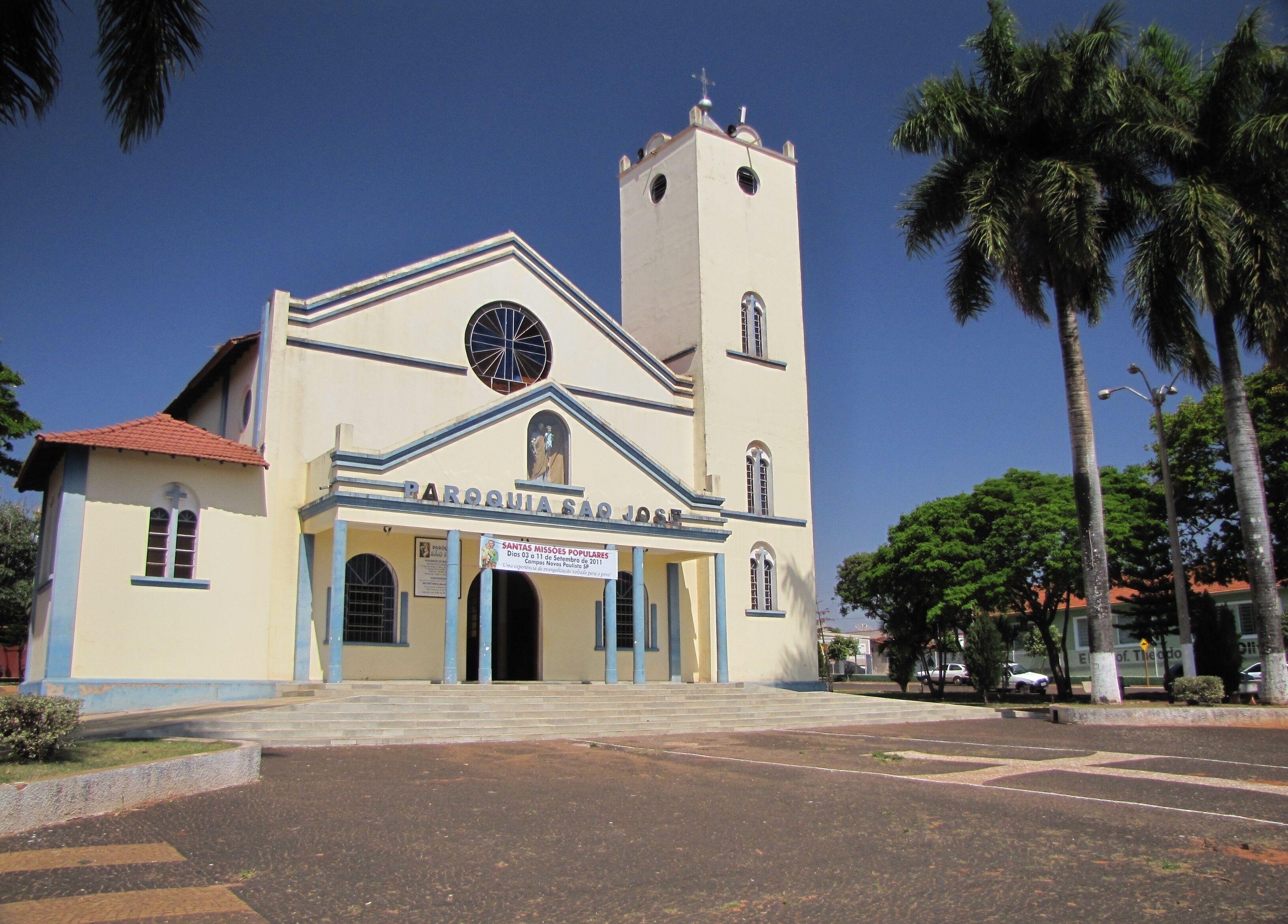 A church with a clock tower and a sign for 'Santas Missoes Populares'.