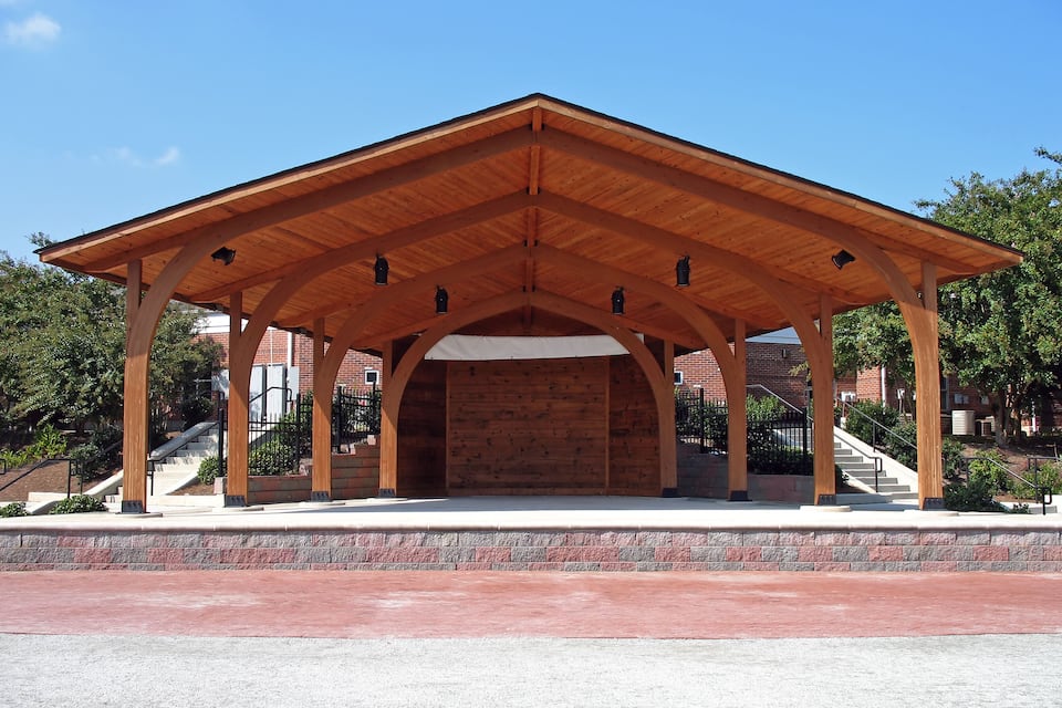 A wooden pavilion with a brick wall, surrounded by a paved area and a staircase.