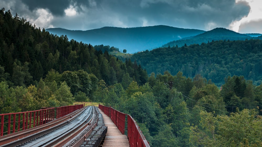 A railway bridge over a forested valley with mountains in the background.