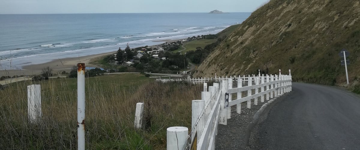 A coastal road with a white fence, grassy hills, and a view of the ocean.