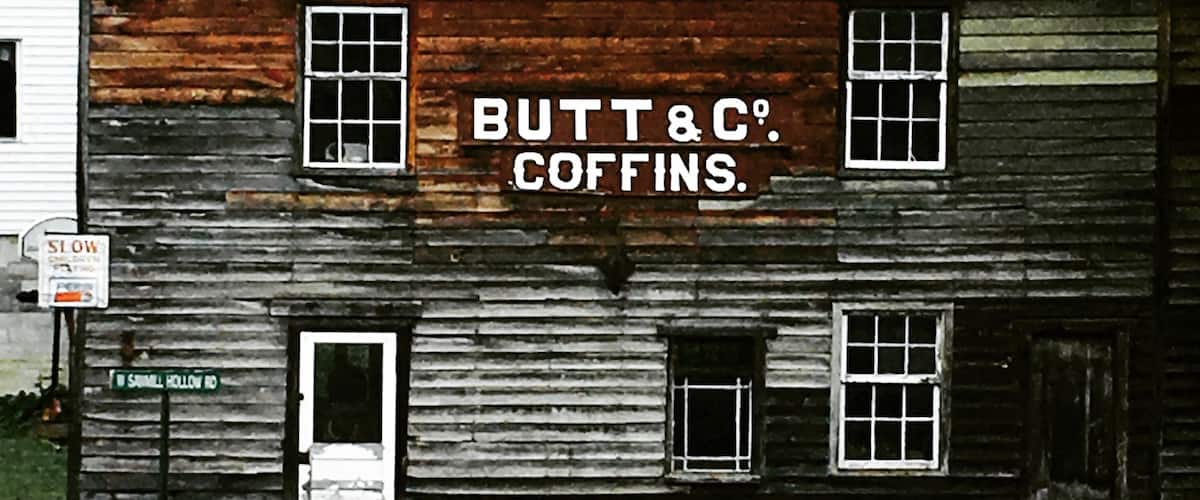A rustic wooden building with a sign that reads "BUTT&C COFFINS."