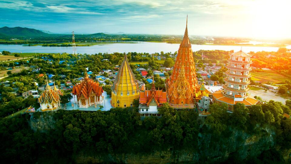 A temple complex with multiple pagodas, surrounded by lush greenery and a river.