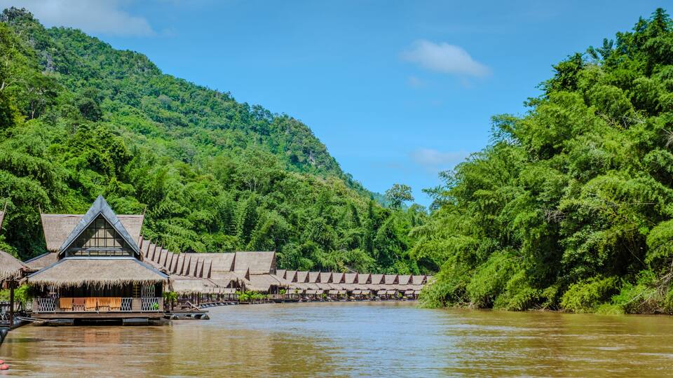 A river with thatched-roof huts and a forested hillside.