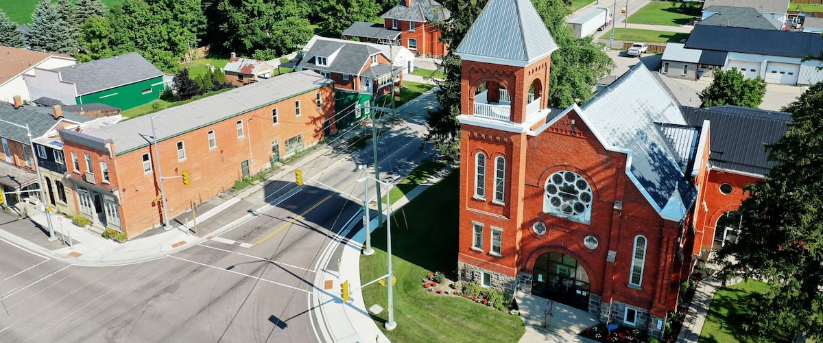 A red brick church with a steeple, surrounded by residential buildings and a green field.