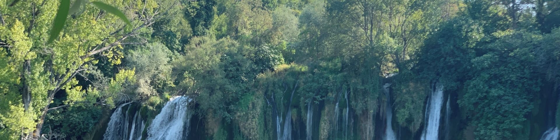 A waterfall cascading into a clear pool surrounded by lush greenery.