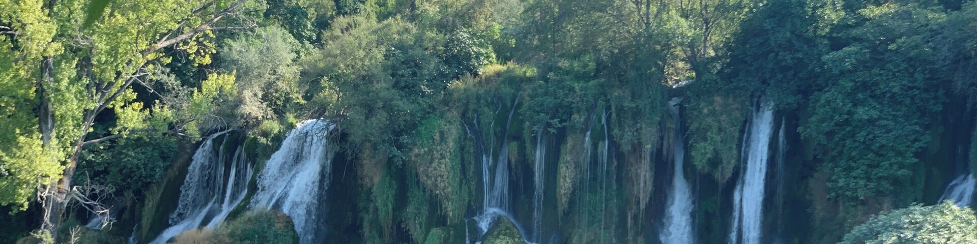 Uma cascata deságua numa piscina límpida, cercada por vegetação exuberante.