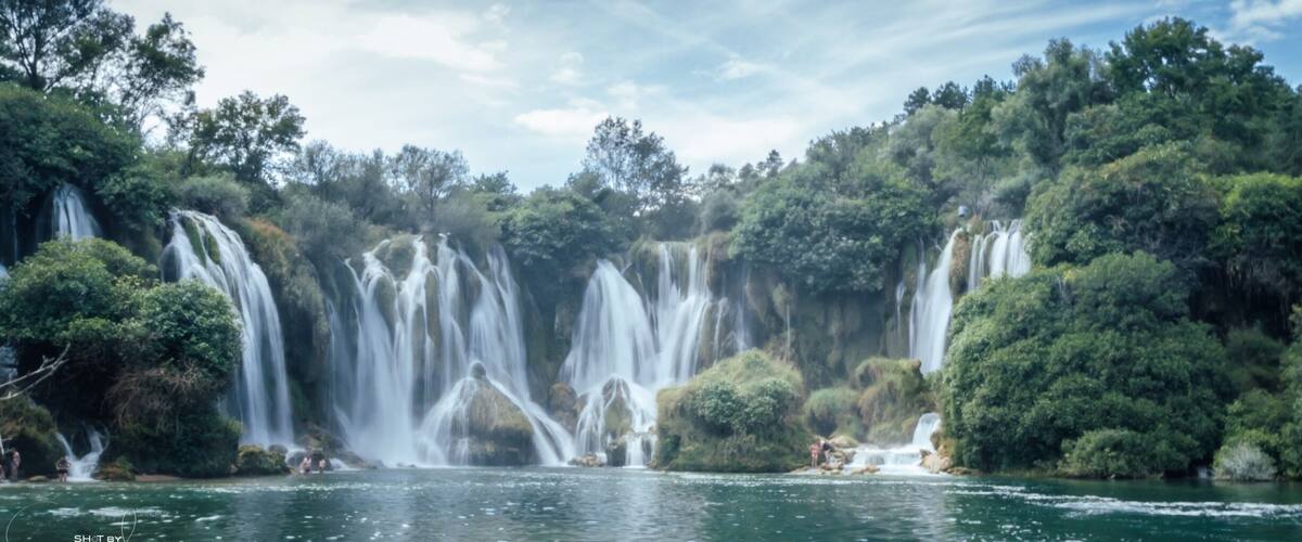 A waterfall cascading into a river surrounded by dense forest.