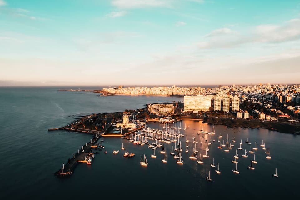 A coastal cityscape with a marina filled with sailboats and a prominent building complex.