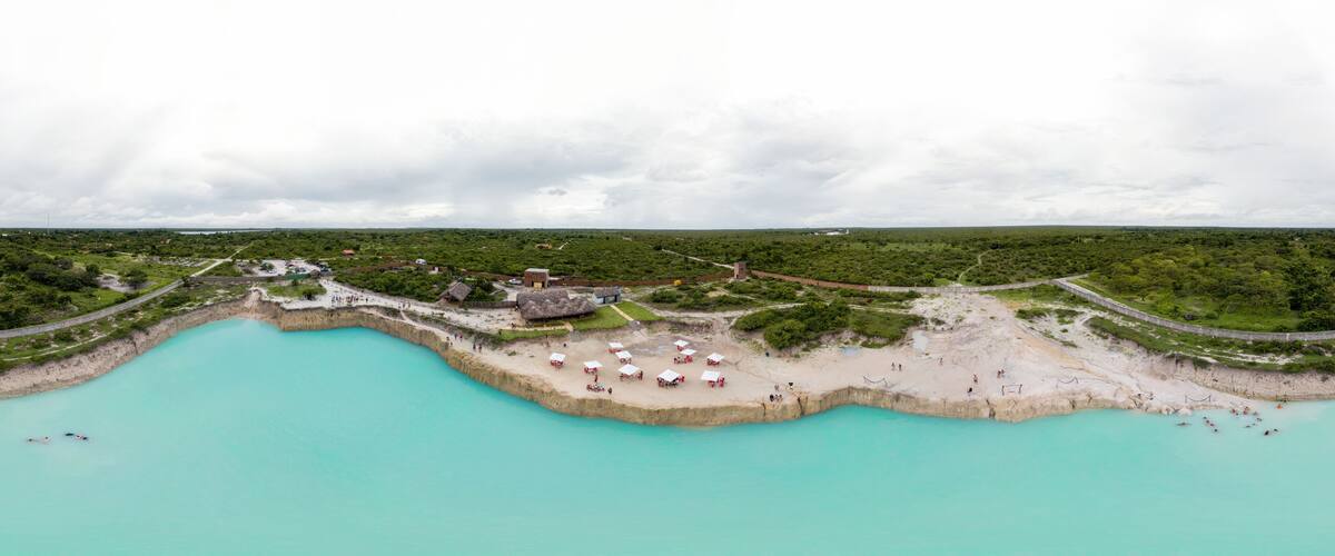 A coastal landscape with a turquoise beach, a thatched-roof structure, and a paved walkway.