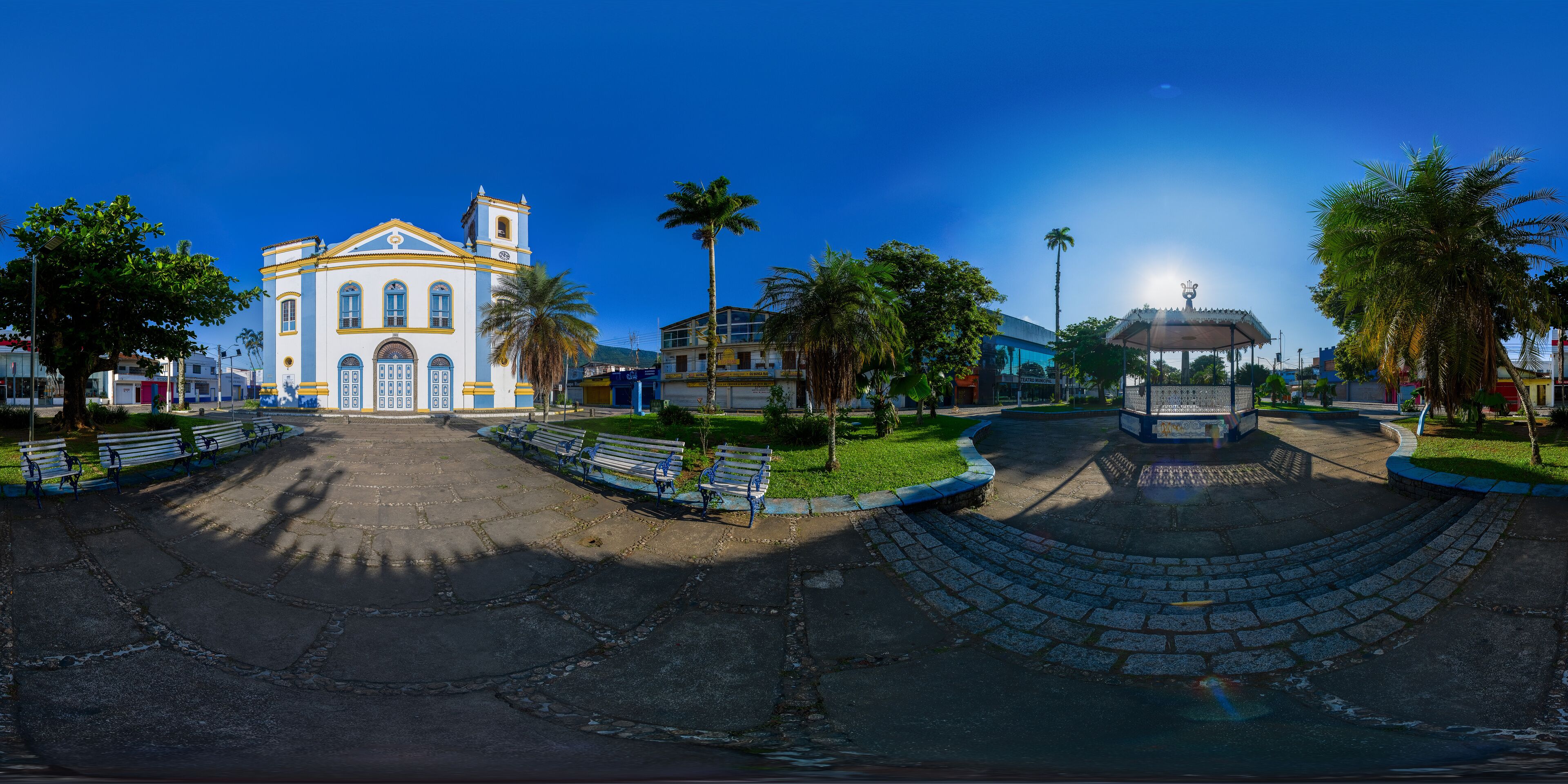 A church with a bell tower, palm trees, benches, and a fountain.