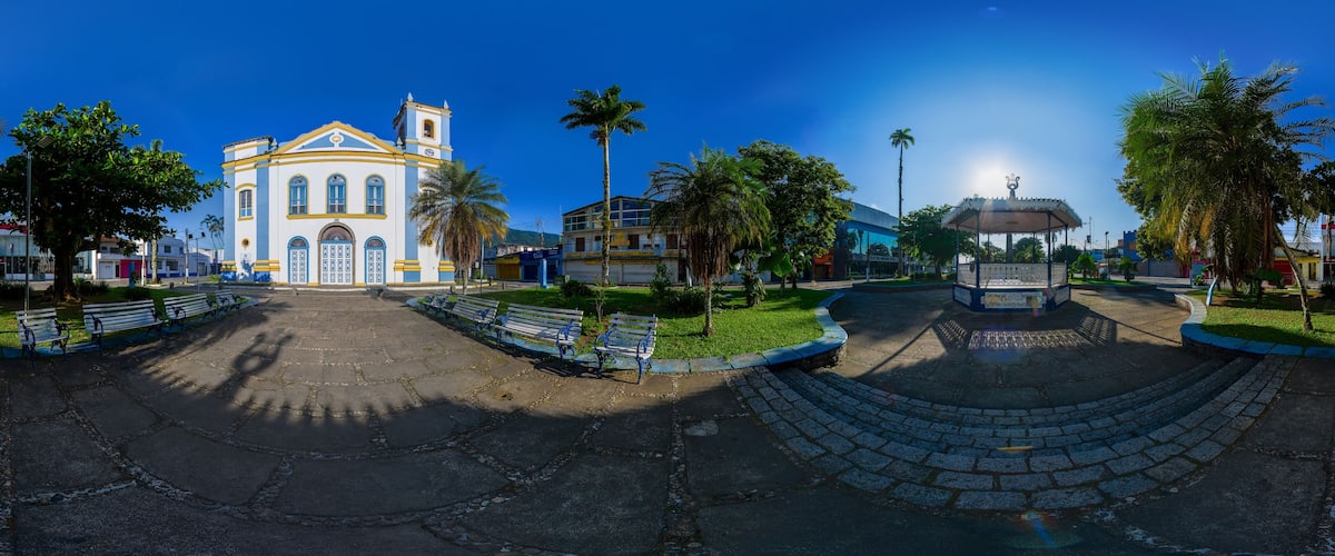 A church with a bell tower, palm trees, benches, and a fountain.