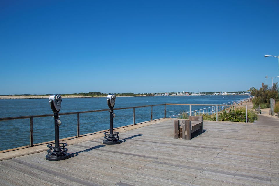 A wooden boardwalk by a body of water with binoculars and a bench.
