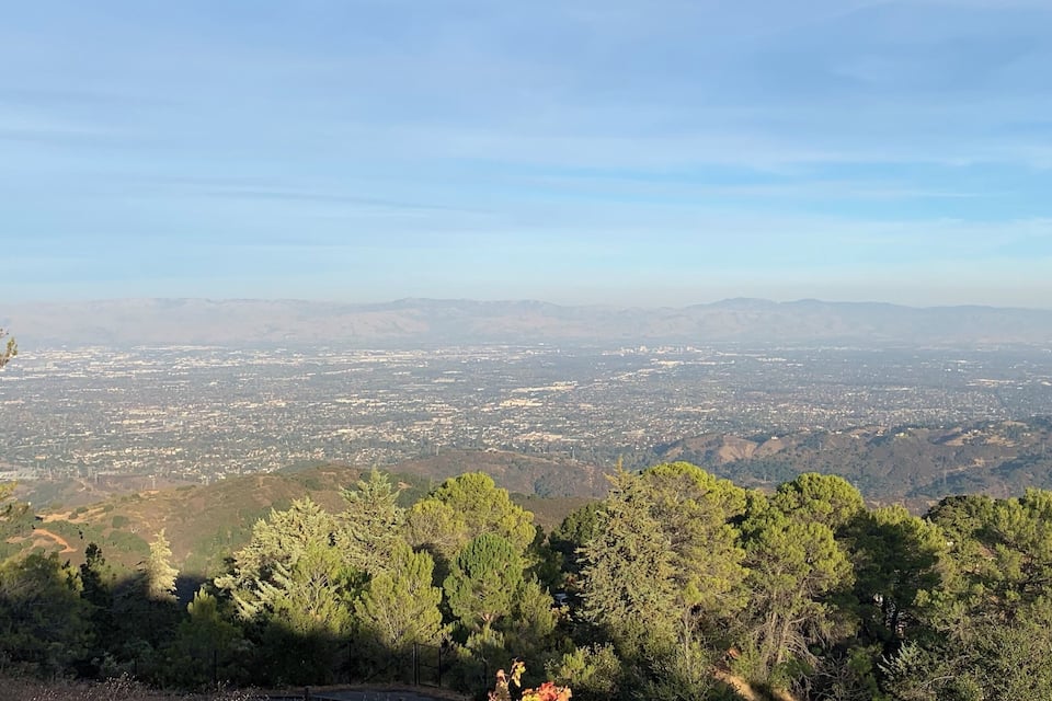 Vista panorâmica de uma cidade, com montanhas ao longe e uma floresta densa em primeiro plano.